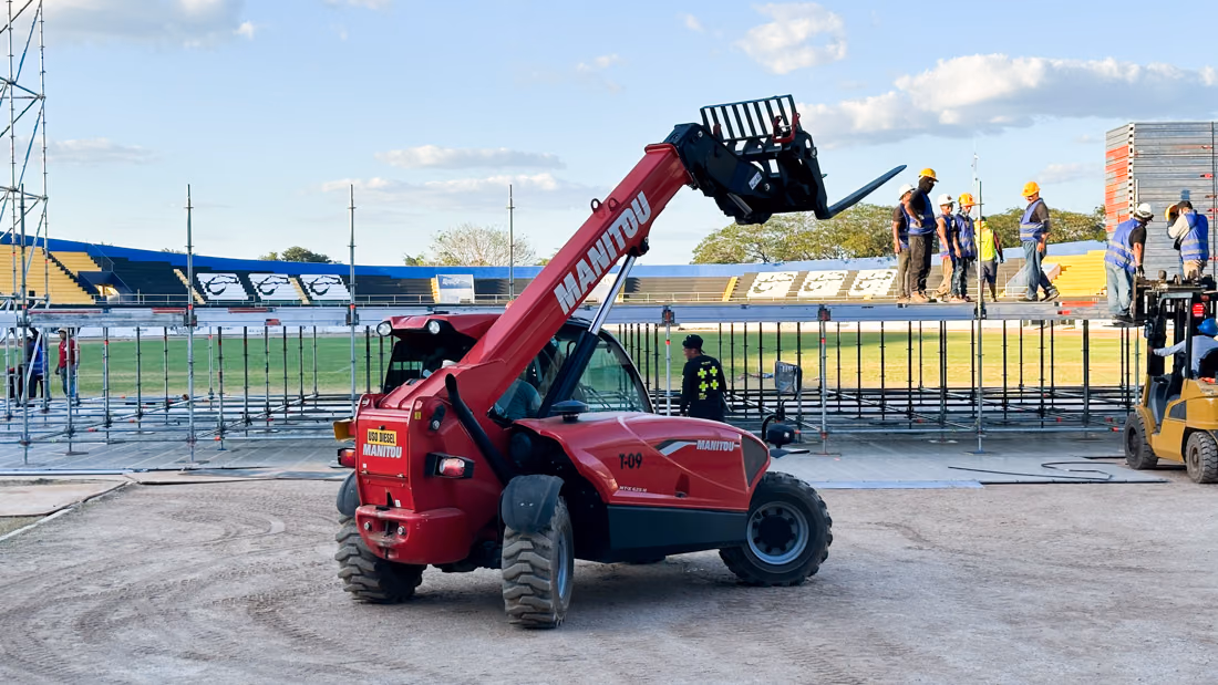 Telehandler Manitou posicionando estructura durante el montaje de un escenario al aire libre